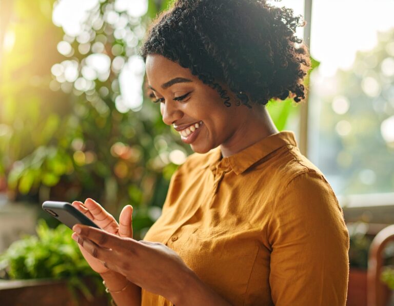 A black woman scrolling social media with plants in the background.